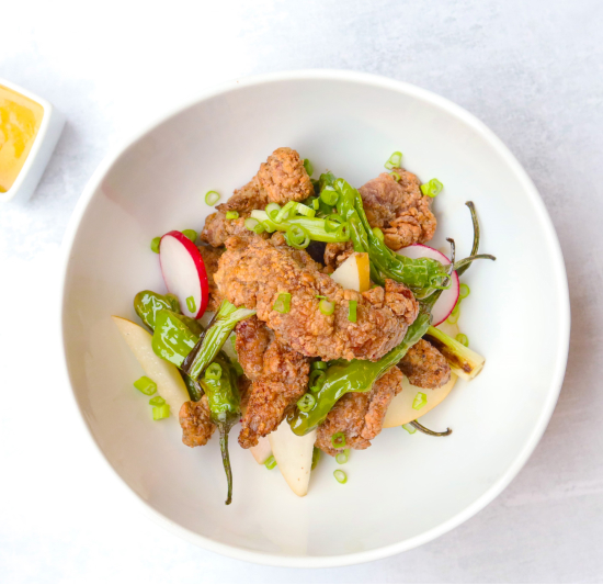 Iberico pork char siu with fried boneless spare ribs, shishito peppers and radishes, in a white bowl on a marble background with dipping sauce in the upper left corner.