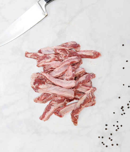 Pile of raw boneless Iberico pork spare rib strips on a marble background with a knife blade and black peppercorns.