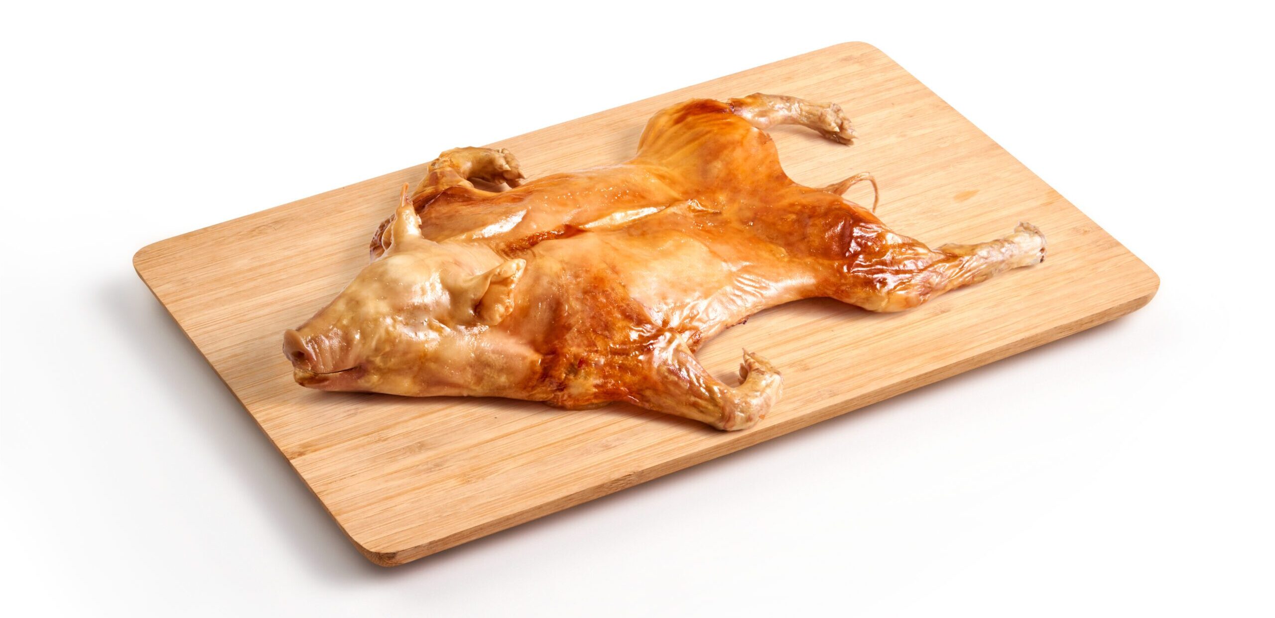 Whole roasted suckling pig splayed on a wooden cutting board.