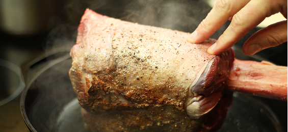 Fingers steady a raw, seasoned Thor’s Hammer beef shank as it is seared in a black cast iron skillet. 