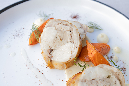 Two slices of deboned, herb-stuffed, roasted rabbit loin are served on a blue-rimmed plate with roasted sweet potatoes, fennel fronds, and dots of white sauce. 