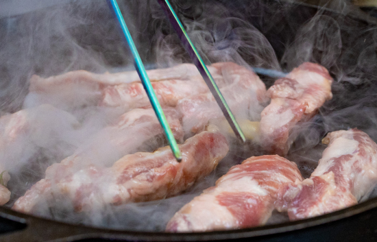 Iberico pork boneless spare ribs searing in a smoky cast iron pan with metal chopsticks.