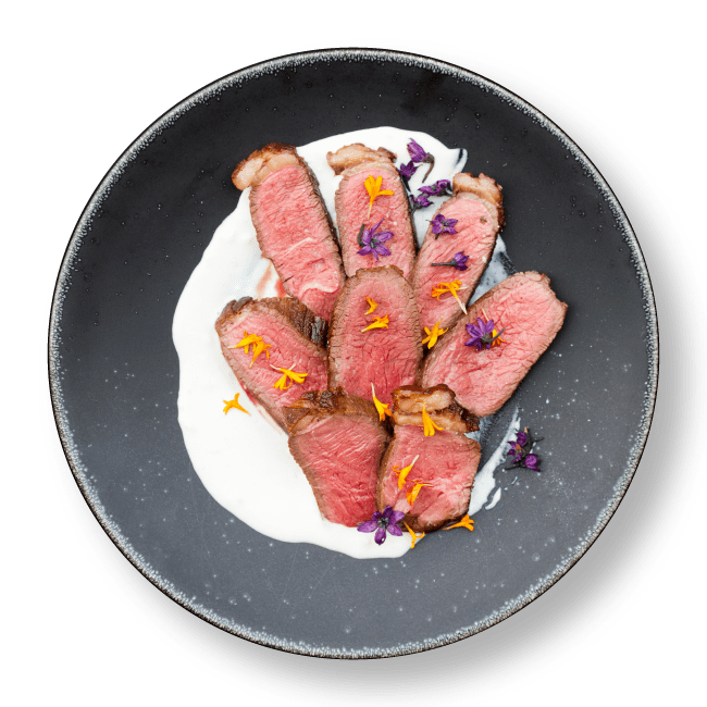 8 slices of seared Silver Fern Farms Angus beef on white sauce with edible flowers in a gray textured bowl