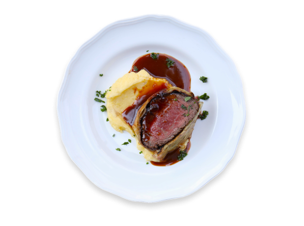 Cooked piece of Ocean Beef with pureed potatoes, brown sauce, and chopped chives on a round white plate.