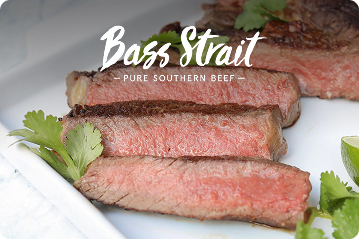 Slices of grass-fed Bass Strait beef with parsley sprigs on a white plate beneath the Bass Strait logo.
