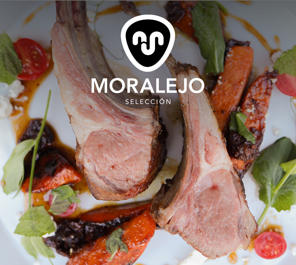 The Moralejo logo superimposed over a white plate holding 2 Merino lamb chops surrounded by glazed yams, sundried tomato, feta, honey, and pea vines.