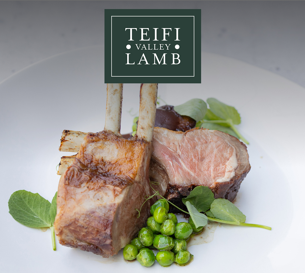 Peas and pea vines are tucked around two double-cut Welsh lamb chops, one propped upright, the other on its side, on a round white plate beneath the Teifi Valley Lamb logo.