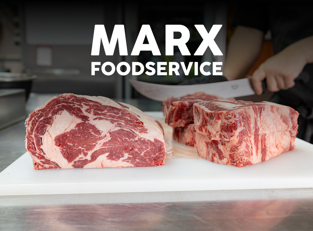 The Marx Foodservice logo is superimposed above a cross-cut section of a raw, boneless ribeye subprimal. Two thick, raw ribeye steaks are stacked on the right. A hand holding a curved knife is slicing more steaks in the background.