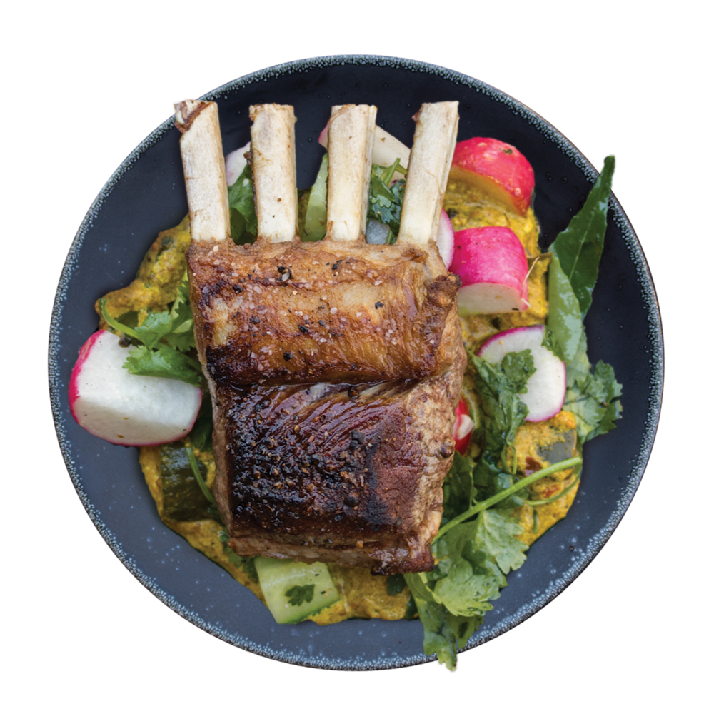 A black bowl containing a cooked rack of Ovation lamb placed on a bed of greens, sliced radishes, and vegetables.