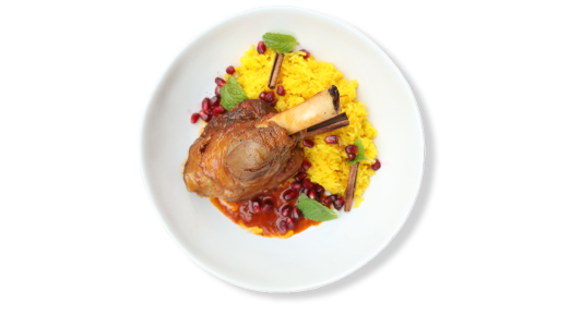 Braised Welsh Hill lamb hindshank served on yellow saffron rice with pomegranates in a white bowl.